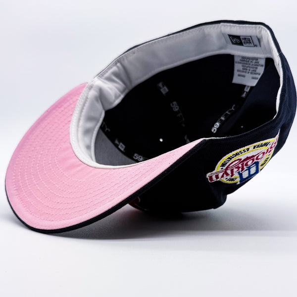 A baseball cap shown from an angled top-down view, featuring a light pink underbrim, a navy blue crown and white guts.