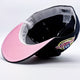 A baseball cap shown from an angled top-down view, featuring a light pink underbrim, a navy blue crown and white guts.