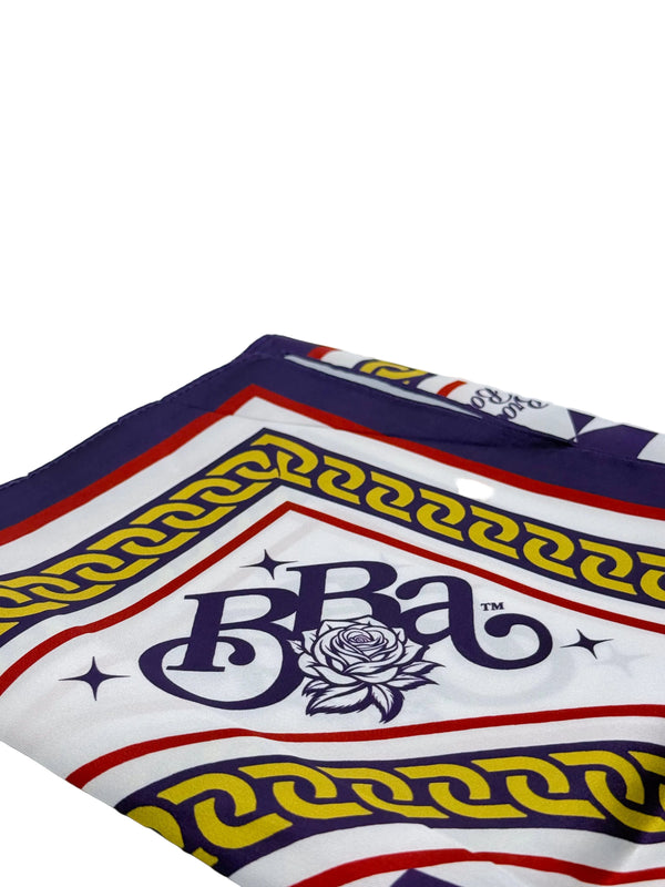 A folded square scarf featuring a white base with a navy blue 'BBA' rose logo, bordered by red and yellow Greek key patterns on a light gray background.
