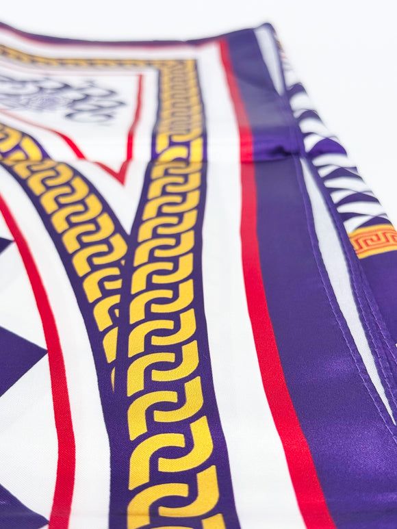 A close-up of a patterned scarf featuring purple, white, red, and yellow Greek key and geometric designs.