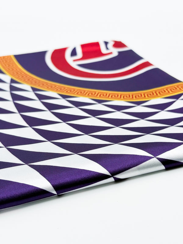 A folded silk scarf featuring a geometric pattern of purple and white triangles, a gold Greek key border, and a red and white circular emblem at the top, displayed on a clean white background.